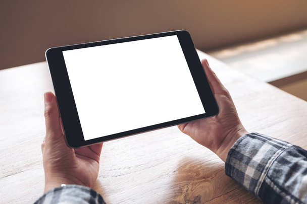 Obrázek rukou držících černý tablet s bílou obrazovkou na dřevěném stole - Fotografie, Obrázek