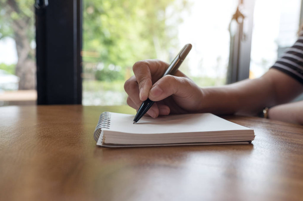 Imagen de cerca de las manos de una mujer anotando en un cuaderno blanco en blanco en la mesa  - Foto, Imagen