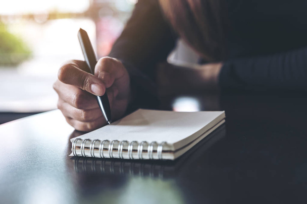 Imagem de perto das mãos de uma mulher escrevendo em um caderno branco em branco na mesa  - Foto, Imagem