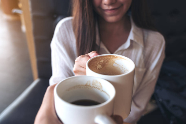 Close up image of a man and a woman clinking white coffee mugs in cafe - Photo, Image
