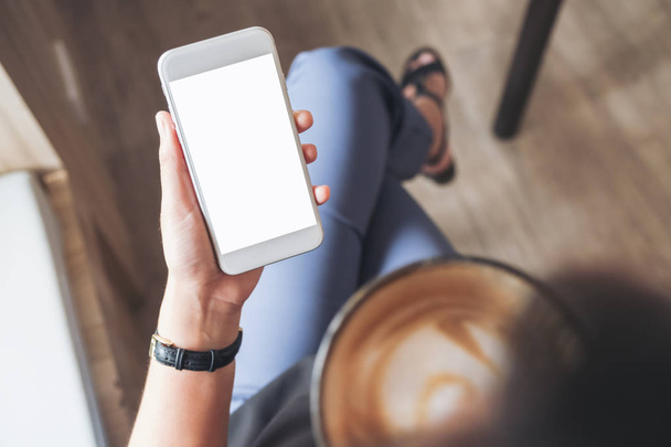 カフェでコーヒーを飲みながら、白い携帯電話を持っている女性の手のモックアップイメージをトップ表示します。 - 写真・画像