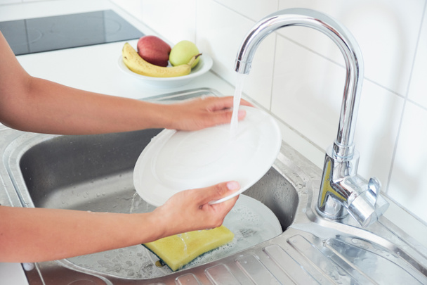 Image recadrée de jolie jeune femme est laver la vaisselle tout en faisant le nettoyage à la maison. - Photo, image