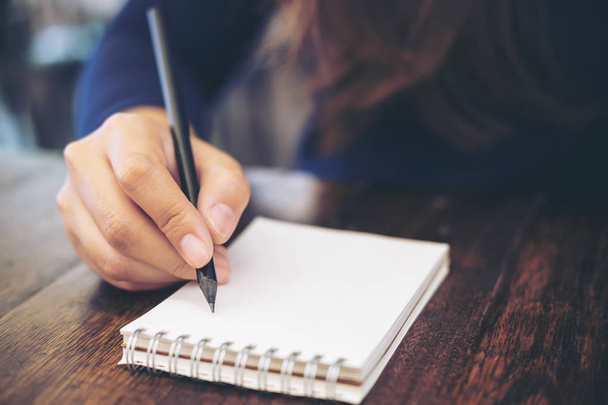 Fechar a imagem da mão da mulher escrevendo no notebook com fundo de mesa de madeira
 - Foto, Imagem