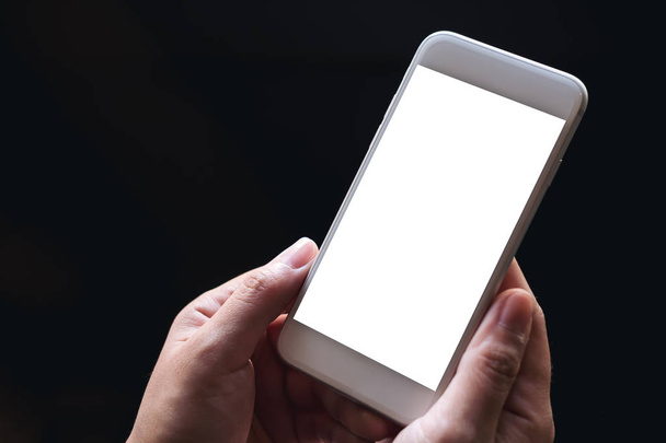 Imagen burlona de manos sosteniendo teléfono móvil blanco con pantalla en blanco con fondo negro
  - Foto, Imagen
