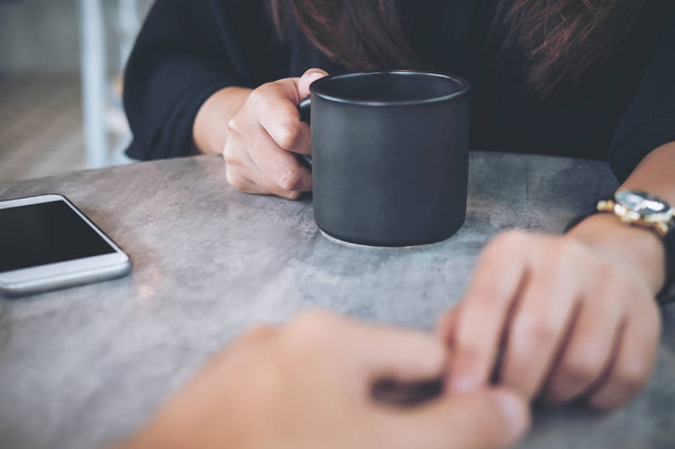 Un hombre y una mujer que se tocan y se cogen las manos con amor, con taza de café y teléfono móvil en la mesa en la cafetería
 - Foto, imagen
