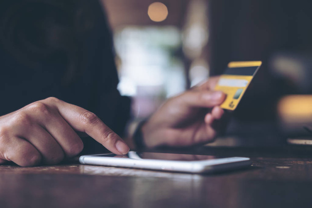 Imagen de primer plano de la mano de una mujer sosteniendo la tarjeta de crédito y presionando en el teléfono móvil en la mesa de madera en la oficina
 - Foto, imagen