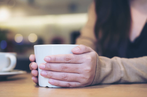 Közelkép kép a nő, kezében egy fehér csésze kávét, és két kézzel, a modern kávézó - Fotó, kép