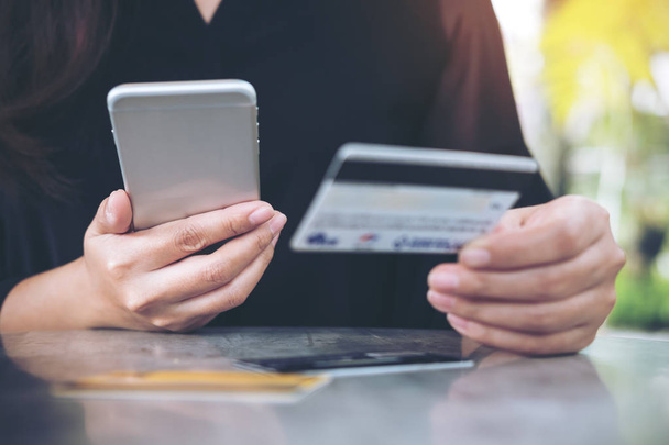 Imagen de primer plano de la mano de una mujer sosteniendo la tarjeta de crédito y utilizando el teléfono móvil en la mesa de la oficina
 - Foto, Imagen