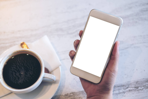 Κοροϊδεύω εικόνα του κινητού τηλεφώνου με κενή, λευκή οθόνη και ένα φλιτζάνι καφέ στο μαρμάρινο τραπέζι στην καφετέρια - Φωτογραφία, εικόνα