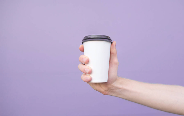 Un vaso de café en la mano de un hombre sobre un fondo púrpura pastel
. - Foto, Imagen