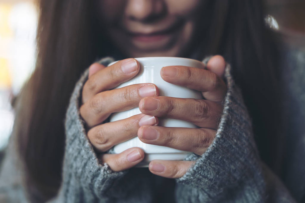 Closeup image of an Asian woman holding and drinking hot coffee in winter time - Zdjęcie, obraz