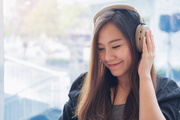 Imagen de cerca de una hermosa mujer asiática disfrutar escuchando música con auriculares en la cafetería moderna con sensación de relax y feliz
 - Foto, Imagen