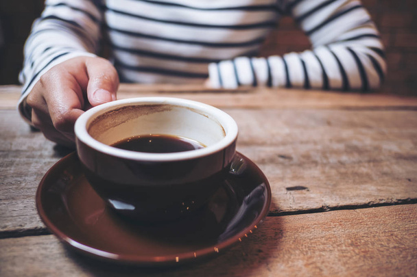 Close-up beeld van een vrouw hand hebt van een kopje koffie op vintage houten tafel in café - Foto, afbeelding