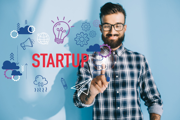 Lächelnder Geschäftsmann im karierten Hemd zeigt auf Start-up-Ikonen - Foto, Bild