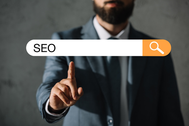 cropped view of professional developer in suit touching SEO search bar - Fotoğraf, Görsel