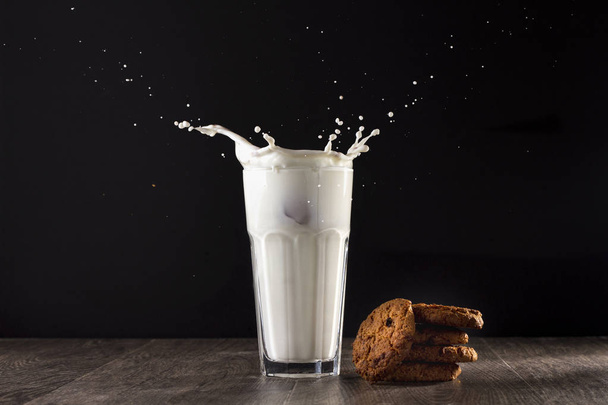 Oatmeal cookies lie on a wooden table on a black background. Near the glass of milk - Фото, зображення