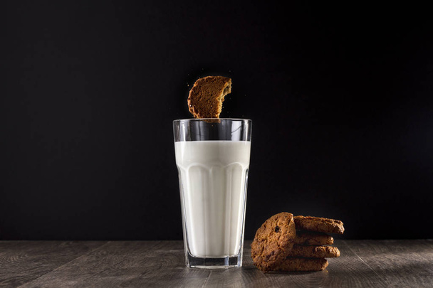 Oatmeal cookies and glass of milk on a wooden table on a black background. - Fotoğraf, Görsel
