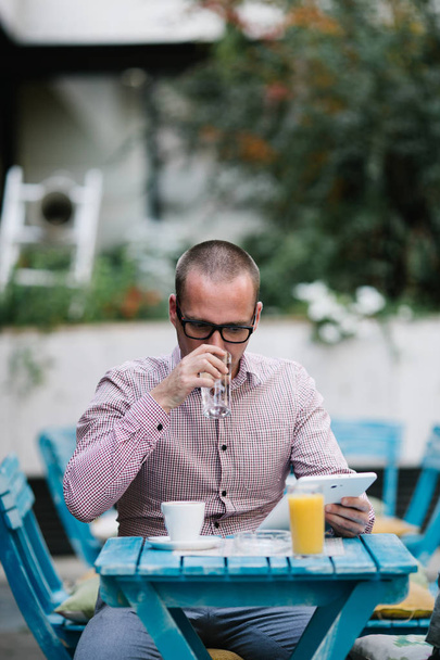 Casually dressed man with eyeglasses sitting in cafe bar, drinking coffee and using tablet. - Photo, image