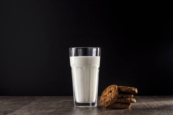 The cookie and glass of milk on a wooden table on a black background. - Fotoğraf, Görsel