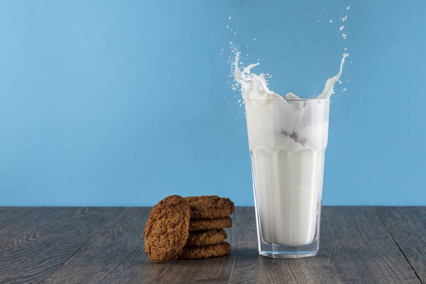Oatmeal cookies lie on a wooden table on a bright background. Near the glass of milk. Spray the milk from the glass - Fotografie, Obrázek