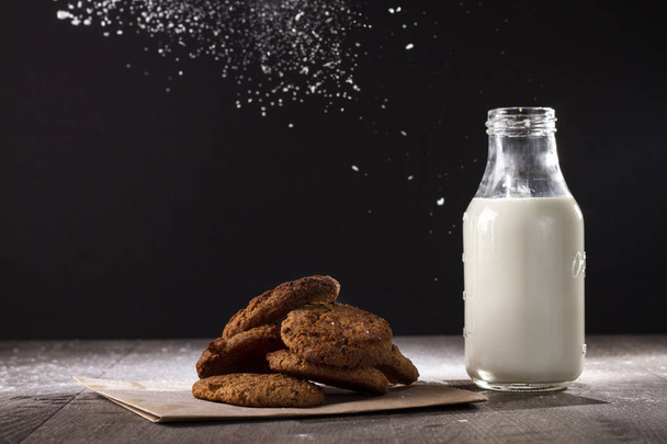 The cookies and milk bottle on a wooden table and sprinkled with powdered sugar. - Photo, image