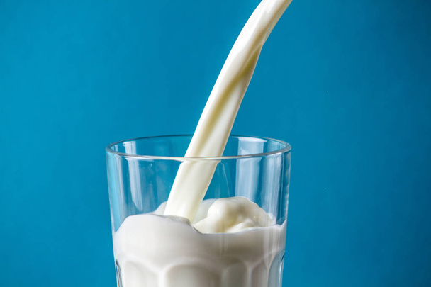 Splashing milk in a glass on a blue background - Photo, image