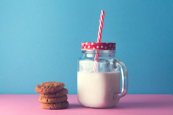Healthy milk in glass jar and cookies on the pink table and on the blue background - Photo, image