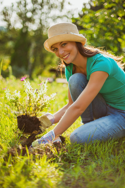 Молода щаслива жінка садить квітку в саду
.  - Фото, зображення