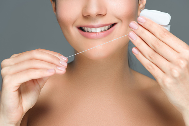 cropped shot of smiling woman with beautiful white teeth and dental floss isolated on grey - Photo, Image