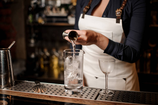 Sexy barman girl pouring vodka into a cocktail glass with ice for making summer drink - Fotó, kép