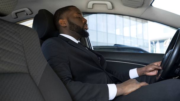 Empresario afro-americano sobrecargado de trabajo sentado en coche, cansado después de un día estresante
 - Foto, imagen