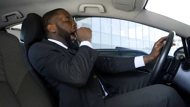Tired black man yawning in car, overworked businessman driving car, danger - Fotoğraf, Görsel