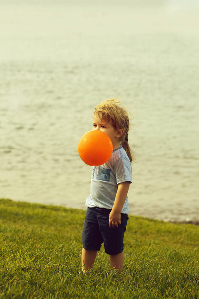 Cute baby boy plays with orange toy balloon - Φωτογραφία, εικόνα