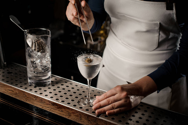 Female barman putting an olive into a cocktail glass filled with fresh summer drink on the bar counter - Фото, зображення