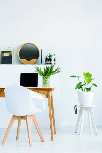 White chair standing by the desk with mockup laptop for remote work in the real photo of bright living room interior with empty wall - Foto, Imagen