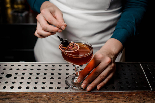 Barman making a strong and sweet summer cocktail decorated with a slice of orange and cherry - Fotó, kép