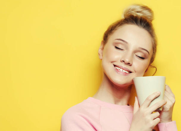 Young woman holding white cup with tea or coffee, lifestyle and food concept. Close up. Yellow background. - Photo, image