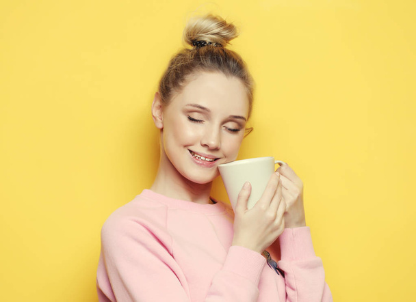 Young blond woman holding white cup with tea or coffee, lifestyle and food concept. Yellow background. - Foto, Bild