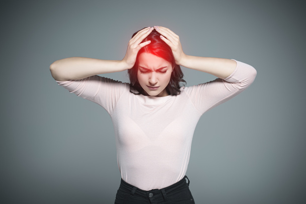 женщина с головной болью и красной болезненной точкой на голове, изолированная от серого
 - Фото, изображение