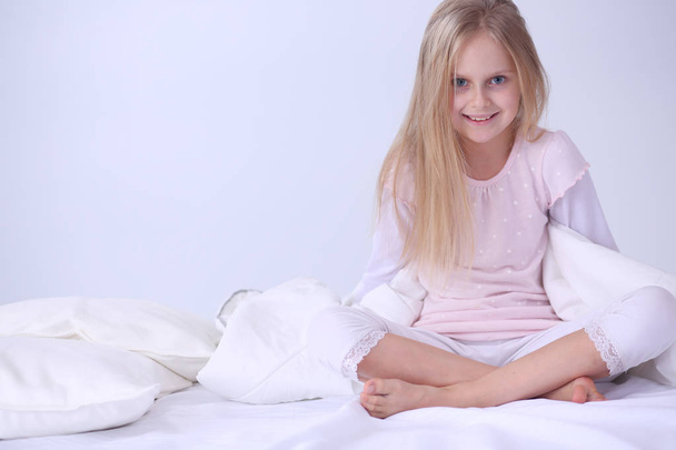 Little girl in the bedroom is sitting on the bed. Little girl is wearing a pajamas and sitting in bed . - Foto, Bild
