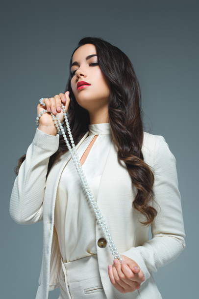bottom view of brunette woman posing in white suit with necklace, isolated on grey  - Photo, Image