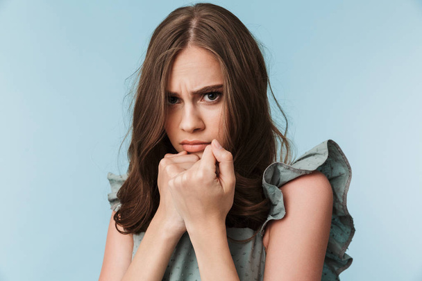 Close up portrait of a scared young woman in dress looking at camera isolated over blue background - Fotó, kép