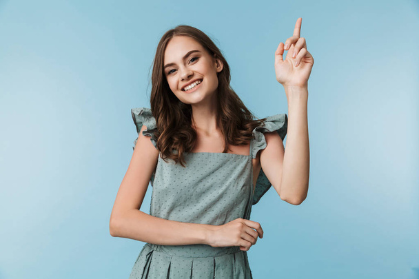 Picture of happy young lady standing isolated over blue background looking camera pointing. - Foto, afbeelding