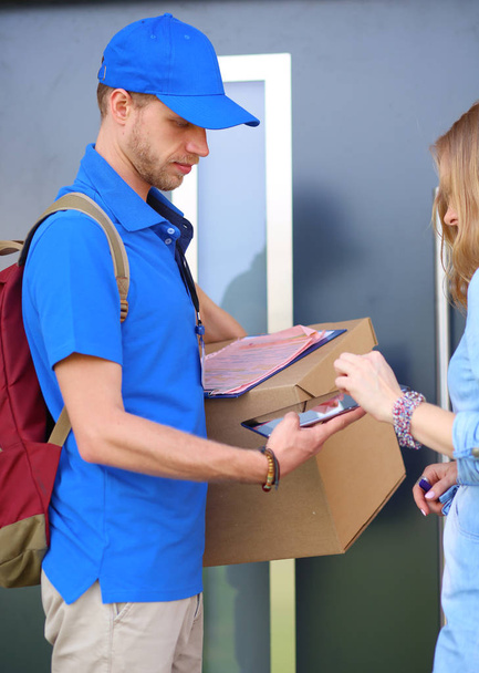 Smiling delivery man in blue uniform delivering parcel box to recipient - courier service concept. Smiling delivery man in blue uniform - Fotografie, Obrázek