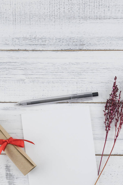 Пустая белая карточка, черная ручка и коричневый свиток украшают фиолетовый сушеный цветок на белом фоне дерева с копировальным пространством, избирательный фокус на белой карточке и ручке
 - Фото, изображение