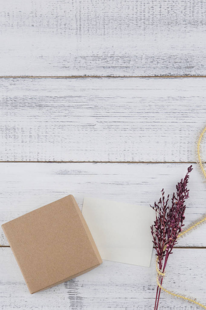 braune Geschenkbox, weiße winzige Karte, braunes Seil und violett getrockneter Blumenstrauß auf weißem Holzhintergrund mit Kopierraum - Foto, Bild