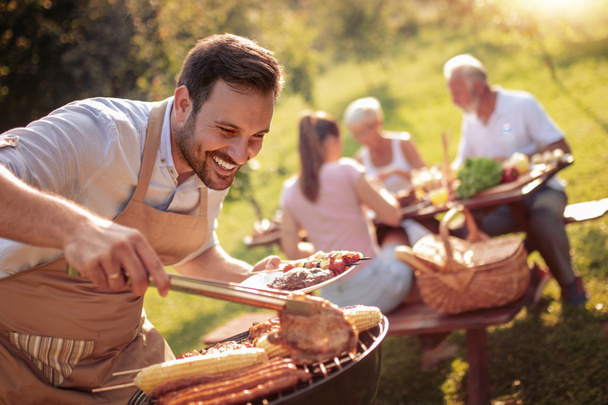 Летнее веселье. Человек готовит мясо на барбекю на летний семейный обед во дворе дома.
. - Фото, изображение
