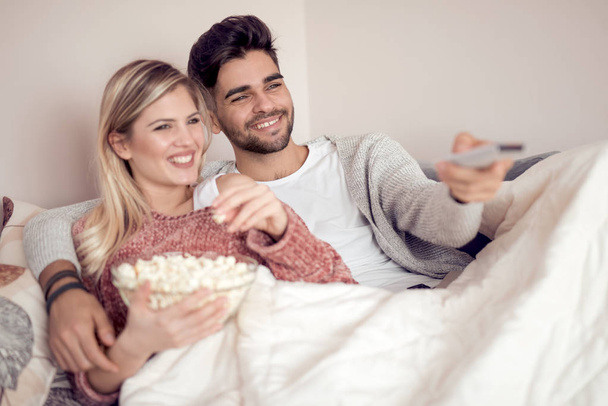 Happy young couple lying on the sofa at home with popcorn and watching TV. - Foto, Imagen