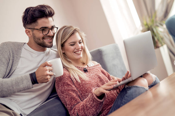Casal jovem usando um laptop enquanto toma um chá em sua sala de estar
. - Foto, Imagem