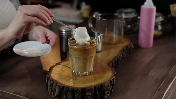Бариста наливает американский кофе в стакан со льдом и добавляет молоко, взбитые сливки и мороженое. бариста готовит кофе фраппе в кафе. Мягкий фокус
 - Кадры, видео